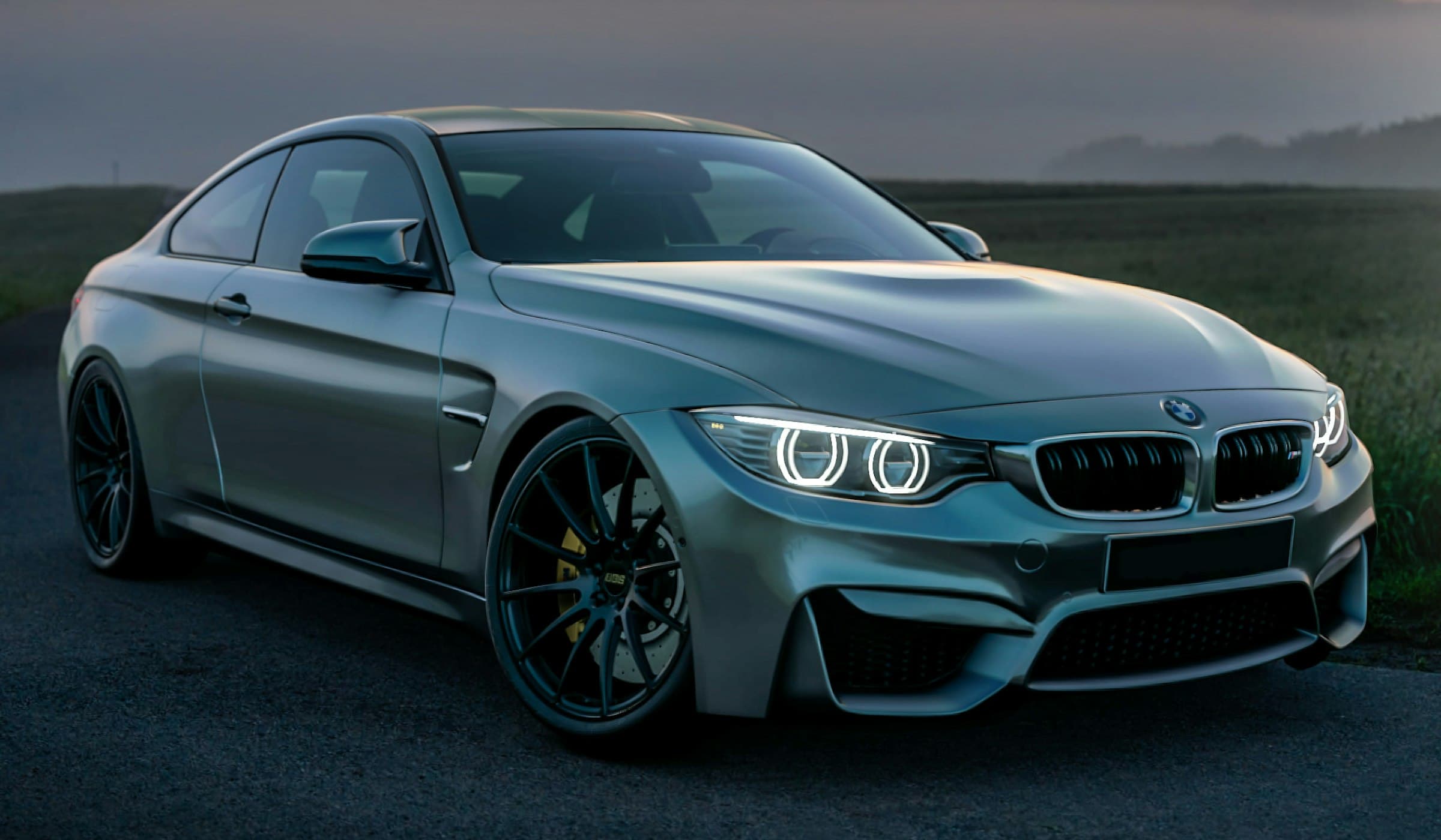 Grey BMW M4 coupé with headlights on, parked at dusk